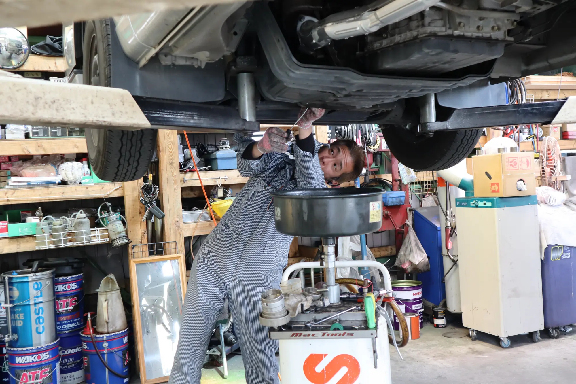 リフトアップした車の下でオイル交換を行う整備士