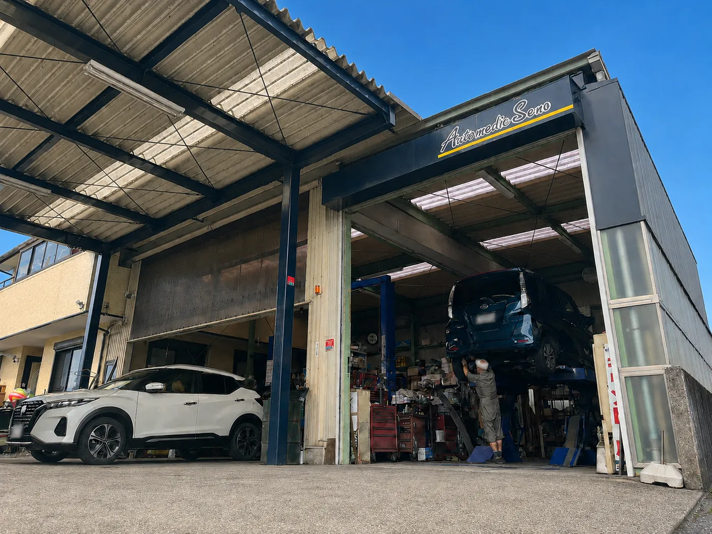 オートメディックセノの工場外観。看板の下でリフトアップした車の整備が行われている